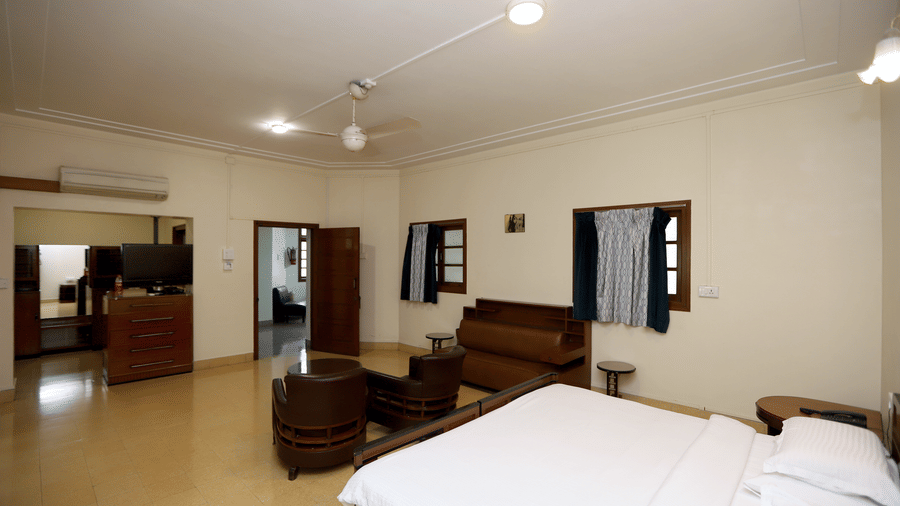 A wide-angle view of a bright guest room featuring white linens, dark wood furniture, and a separate sitting area | Trance Sunderban Resort