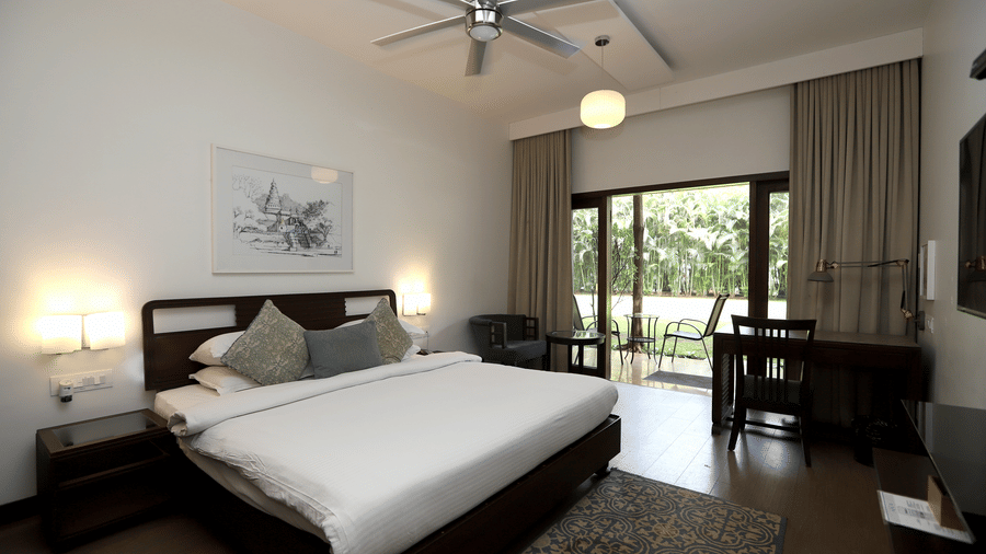 A bright room featuring a king size bed, dark wood furniture, and glass sliding doors leading to a private balcony | Trance Sunderban Resort