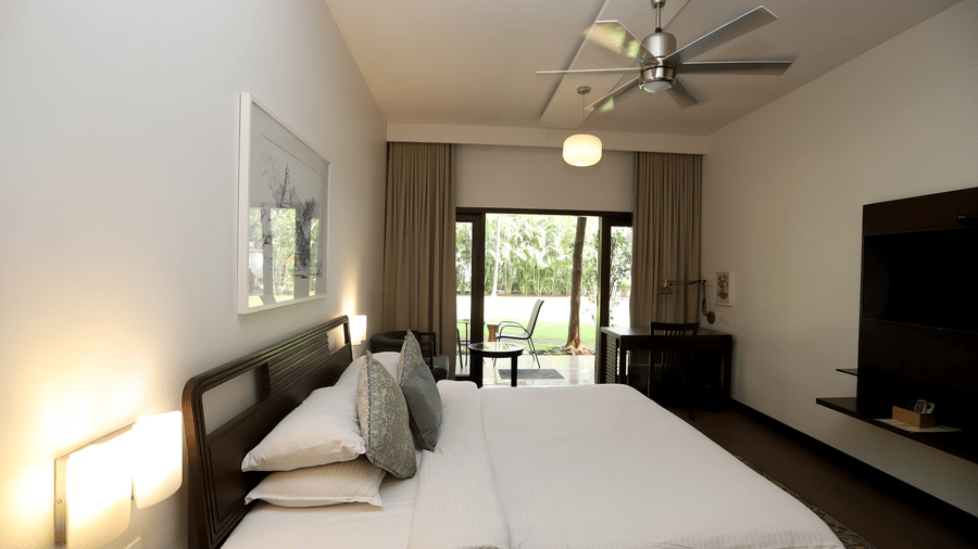 A cosy perspective of the bed with soft headboard lighting, looking out toward the balcony and garden view | Trance Sunderban Resort