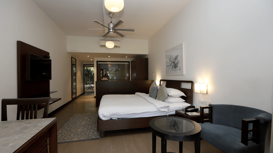 A Studio bedroom featuring twin beds pushed together, warm red-toned flooring, and a large dark wood armoire | Trance Sunderban Resort