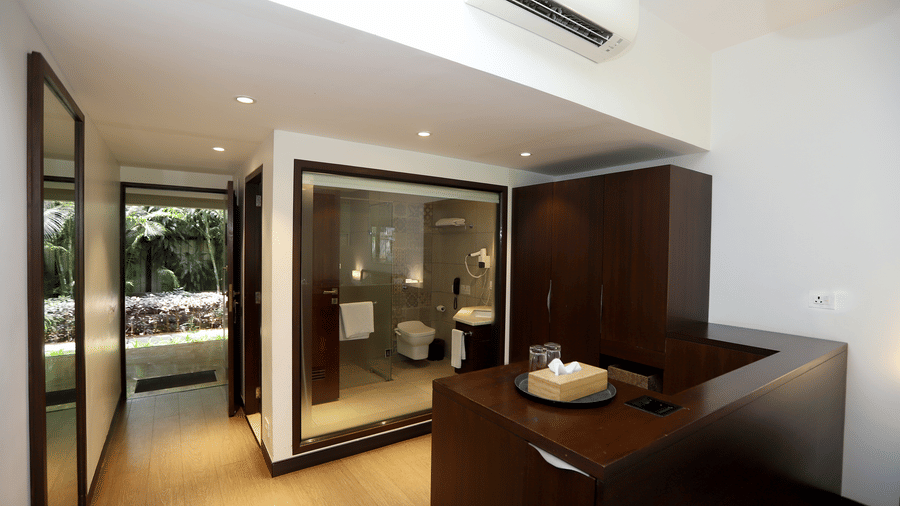 A sleek view showing a dark wood wardrobe and a glimpse into a glass-walled contemporary bathroom | Trance Sunderban Resort
