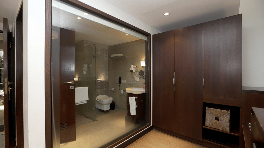 A view of the modern ensuite featuring a large glass partition, dark wood cabinets, and integrated storage | Trance Sunderban Resort