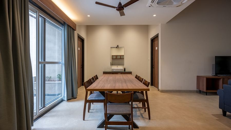 Ananta Garden Villa dining area with a long wooden table, chairs, and a fan, offering a view of the resort's interior.