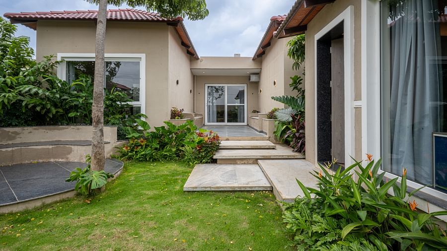Ananta Garden Villa's exterior showing a well-maintained green lawn, stepping stones, and lush foliage, leading to the entrance of the villa.