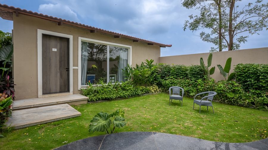 Ananta Garden Villa exterior showing the villa building, a lush green garden with outdoor seating, and cloudy sky.
