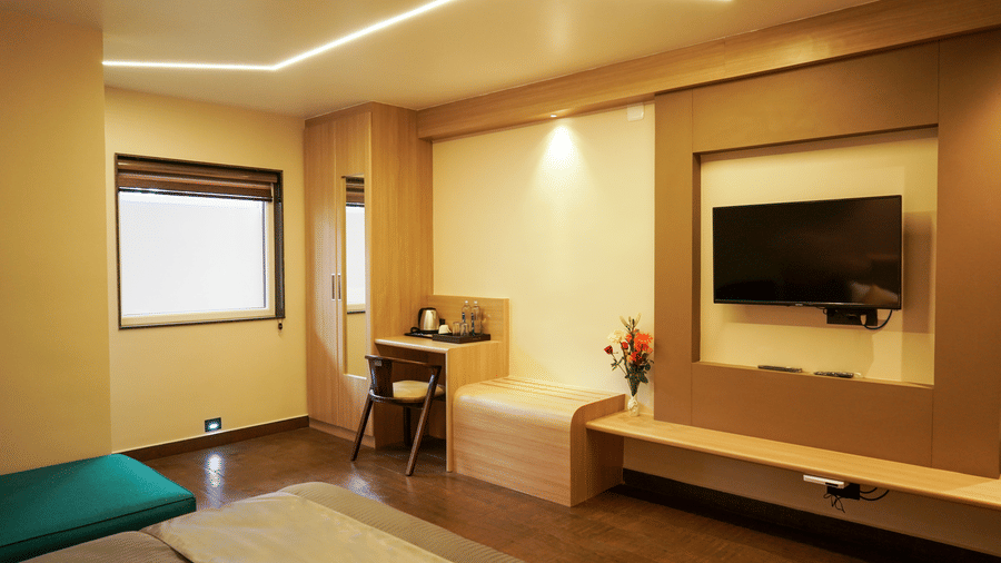 Bright hotel room with a workspace desk, window, wall-mounted TV, and sleek wooden furniture in a contemporary design at Trident The Boutique Hotel, Ooty.