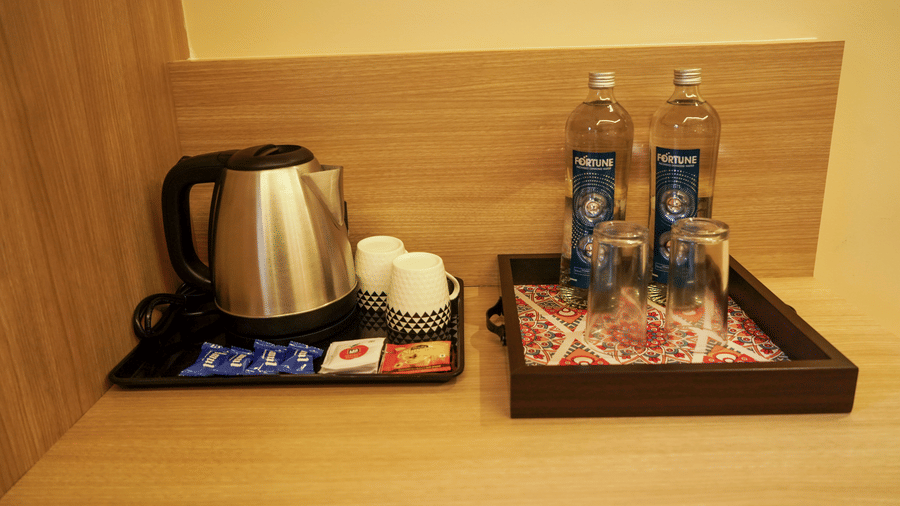 Close-up of a hotel room hospitality tray featuring a stainless steel kettle, ceramic mugs, and bottled water on a wooden surface at Trident The Boutique Hotel, Ooty.
