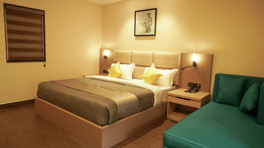 Stylish hotel bedroom with a large double bed, yellow accent cushions, a teal chaise longue, and warm, ambient lighting at Trident The Boutique Hotel, Ooty.