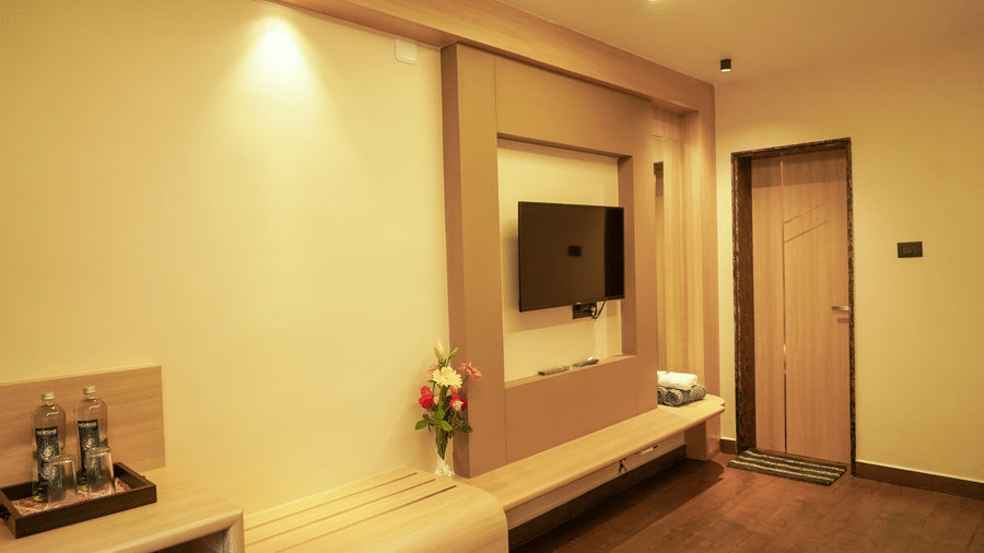 A modern hotel room interior featuring a wall-mounted television, wooden panelling, and a minimalist desk with bottled water at Trident The Boutique Hotel, Ooty.