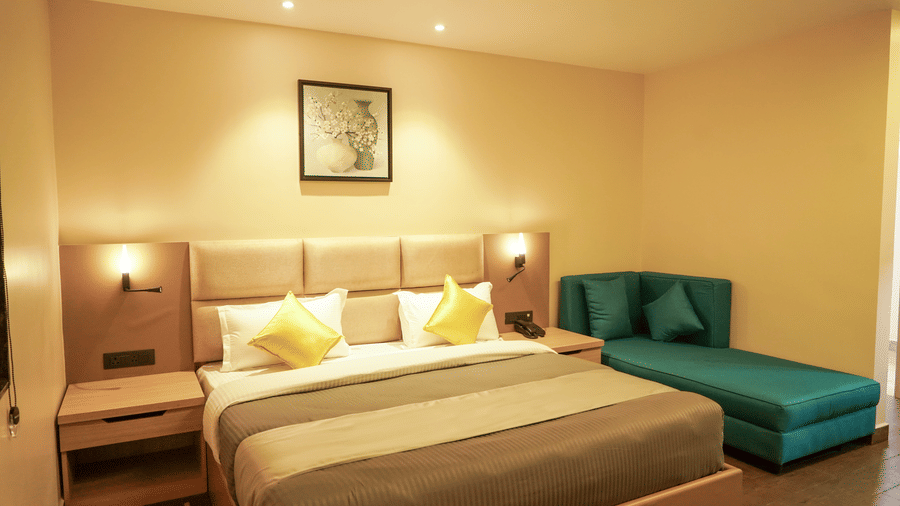 A stylish hotel bedroom featuring a double bed with yellow cushions and a teal chaise longue under warm lighting at Trident The Boutique Hotel, Ooty.