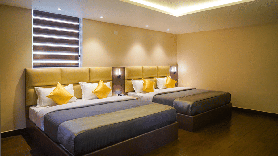 Contemporary hotel room with two double beds, yellow cushions, padded headboards, and warm recessed lighting at Trident The Boutique Hotel, Ooty.