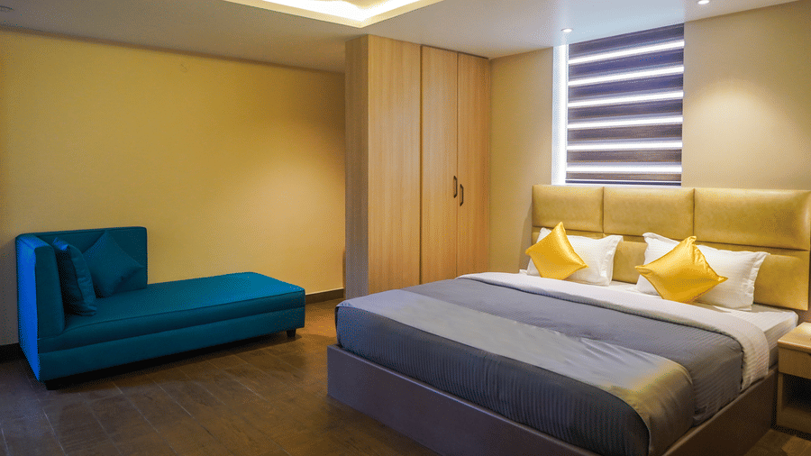 Modern hotel bedroom featuring a double bed with yellow cushions, a teal chaise longue, and warm ambient lighting at Trident The Boutique Hotel, Ooty.