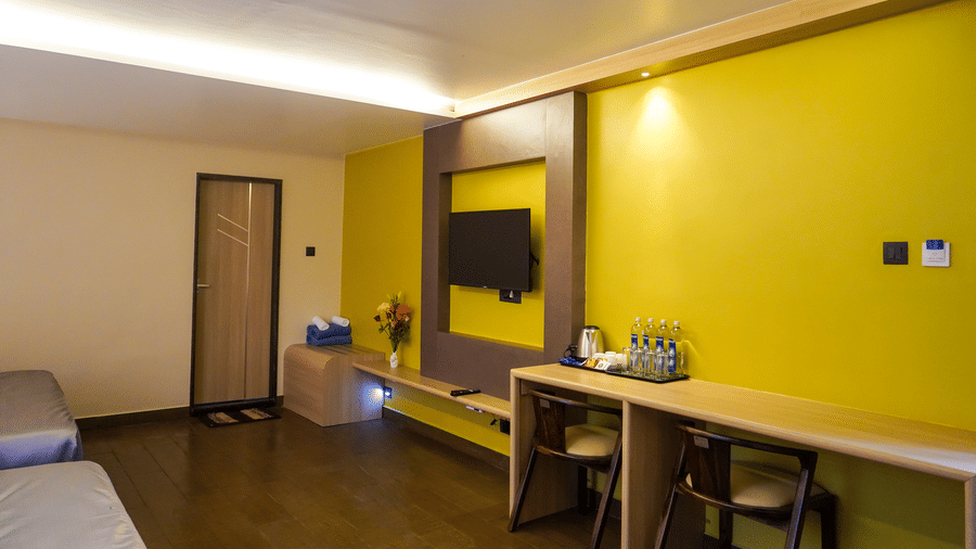 Minimalist workspace with a vibrant yellow feature wall, wall-mounted TV, and wooden desk with chairs at Trident The Boutique Hotel, Ooty.