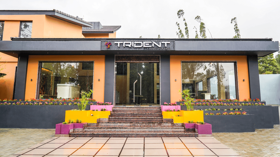 Symmetrical frontal view of a modern building entrance featuring colourful planters and wide glass doors at Trident The Boutique Hotel, Ooty.