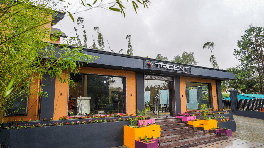 Ground-level view of a modern building facade featuring large glass windows and minimalist architectural design at Trident The Boutique Hotel, Ooty.