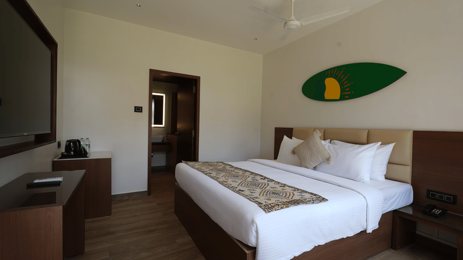 Minimalist room with double bed, side tables, television and wooden flooring at Trishvam Palolem Beach Resort, Goa.