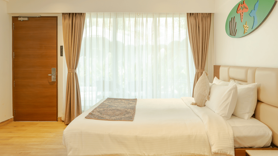 A bedroom at Trishvam Palolem Beach Resort, Goa featuring a double size bed, a big abstract art frame on the wall, and a window covered with curtains.