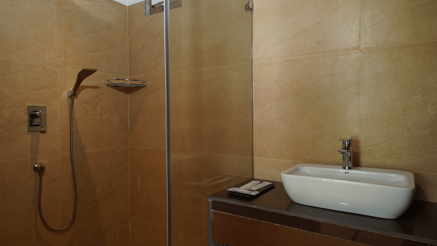 Modern bathroom with glass shower, wall-mounted basin and warm lighting at Trishvam Palolem Beach Resort, Goa.