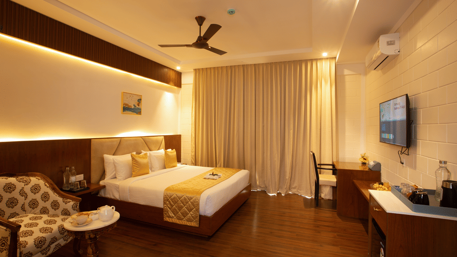 Hotel room with large bed, yellow accents, armchair, desk, and wall-mounted television