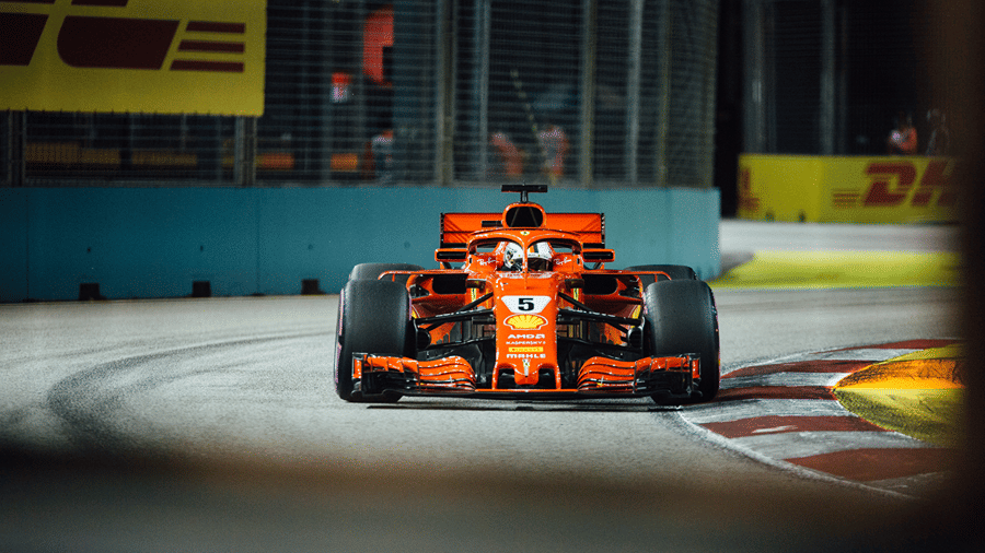 A close-up shot of a bright orange Formula 1 racing car driving fast on a circuit track with sponsors in the background.