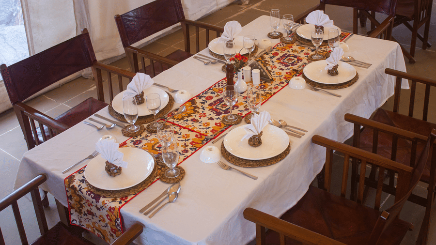 Overhead view of a beautifully arranged dining table decorated with an intricate, colorful patterned table runner and elegant plates - Umaria Safari Camp