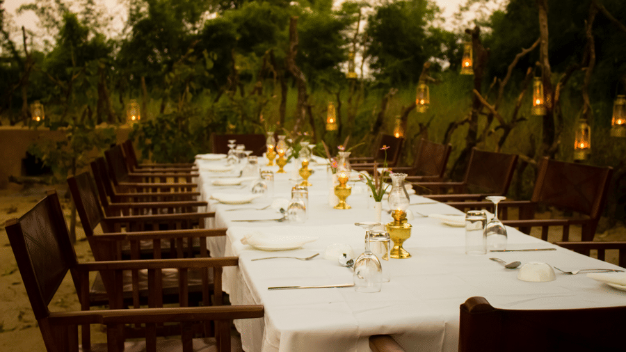 A beautifully arranged long dining table lit with candles and lanterns for a formal evening dinner outdoors - Umaria Safari Camp