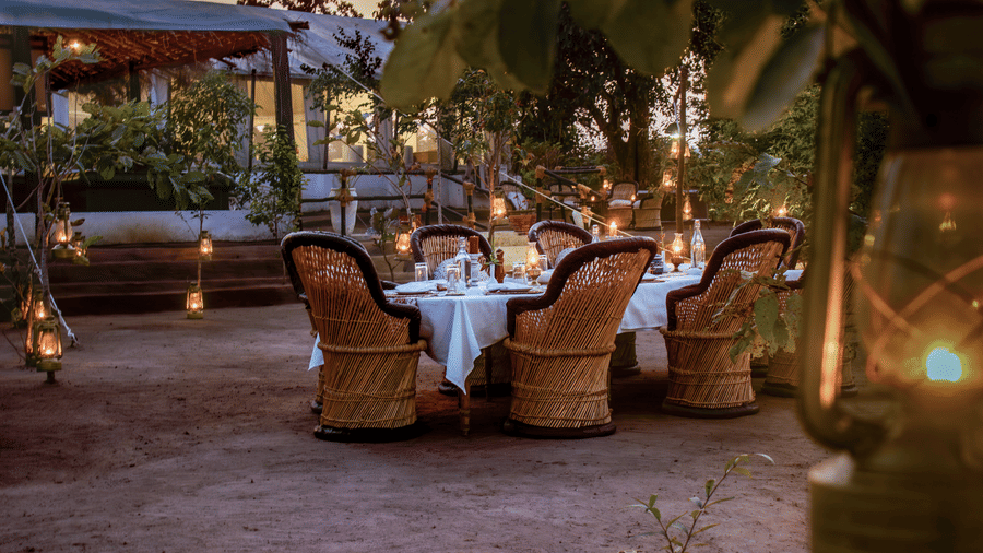 An enchanting outdoor dining arrangement at twilight with woven wicker chairs around a table illuminated by ambient lanterns - Umaria Safari Camp