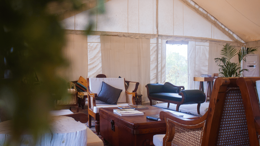 Spacious interior lounge area inside a luxury tent featuring wooden armchairs, plush sofas, and elegant rustic decor - Umaria Safari Camp