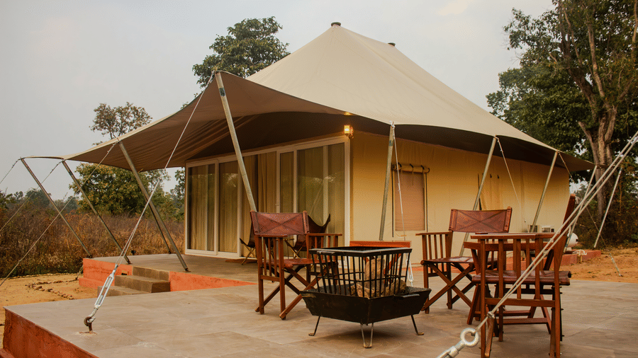 Outdoor seating area with wooden folding chairs arranged on a stone patio in front of a luxury safari tent - Umaria Safari Camp