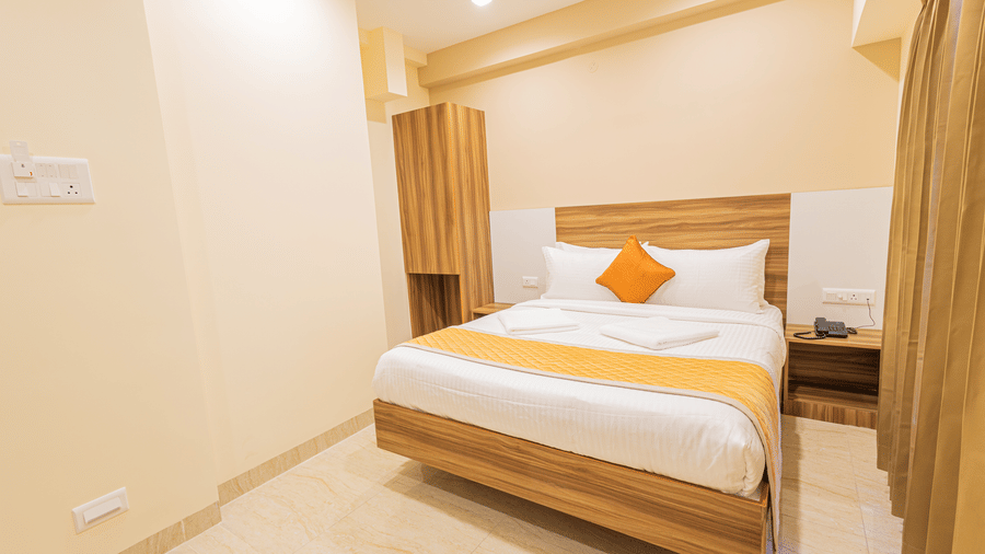 A clean hotel bedroom featuring a wooden bed frame and a wall-mounted air conditioner - Urban Comforts