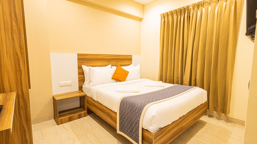 A minimalist bedroom with a double bed, bedside table, and gold-coloured curtains - Urban Comforts