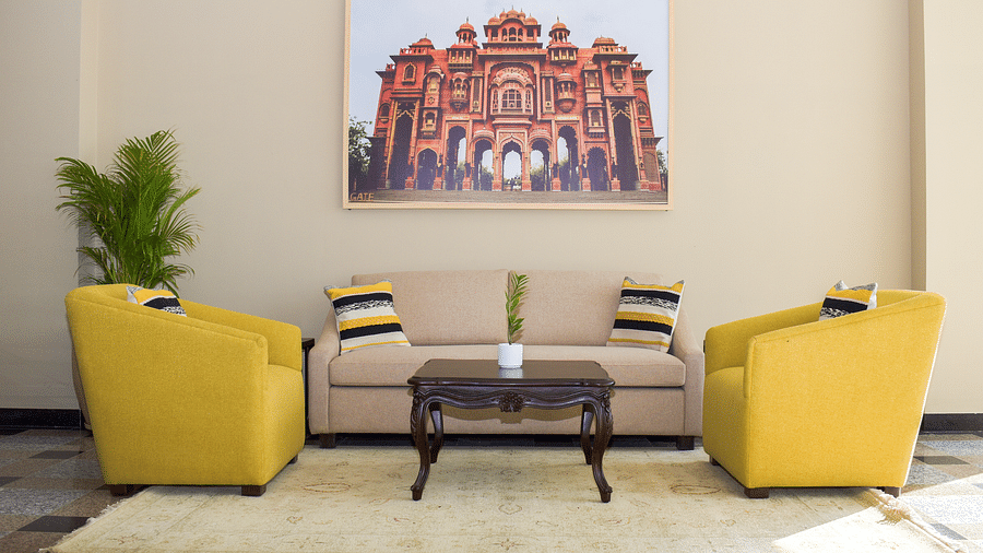 A hotel lobby seating area with yellow armchairs, a beige sofa, a dark wood coffee table, a framed image of a building, and a potted plant - Urban Suites by BluSalzz, Jaipur