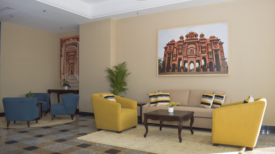 A hotel lobby with a beige sofa, yellow and blue armchairs, a coffee table, and a large framed image of an Indian palace - Urban Suites by BluSalzz, Jaipur