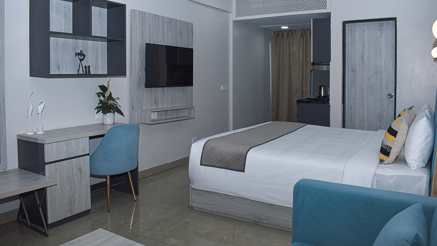 A hotel room with a bed, a blue sofa, a desk and chair, a wall-mounted TV, a kitchenette area, and a wall cabinet - Urban Suites by BluSalzz, Jaipur