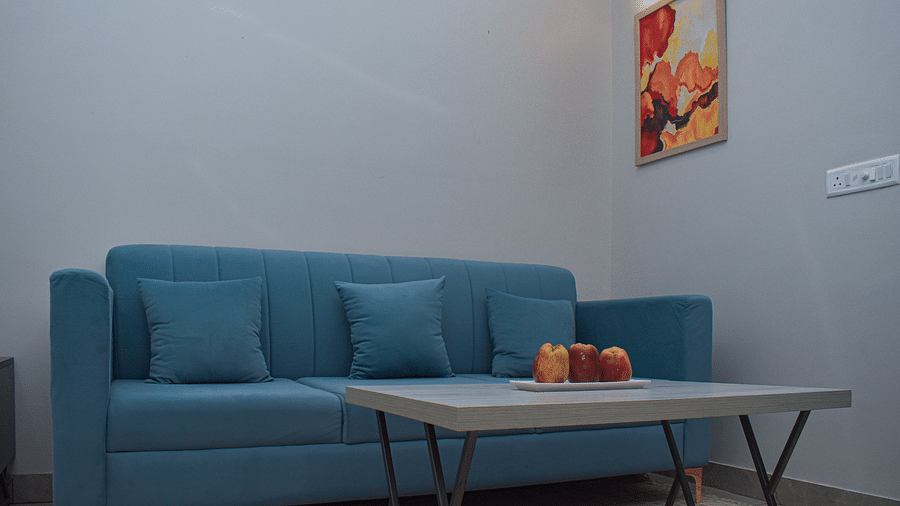 A room with a blue sofa, a light wood coffee table with fruit, and a framed abstract artwork on the wall - Urban Suites by BluSalzz, Jaipur