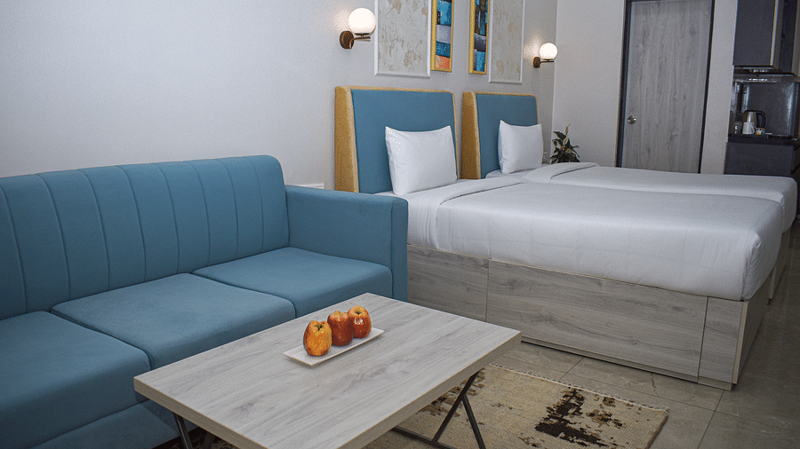 A hotel room with two twin beds, a blue sofa, a light wood coffee table with fruit, and a kitchenette area - Urban Suites by BluSalzz, Jaipur