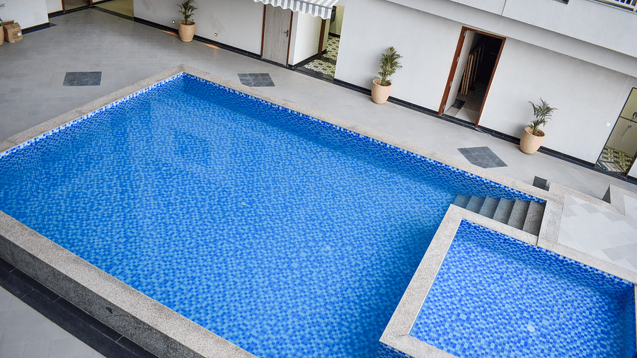 An outdoor swimming pool with blue tiles, surrounded by a concrete patio, potted plants, and building exteriors - Urban Suites by BluSalzz, Jaipur