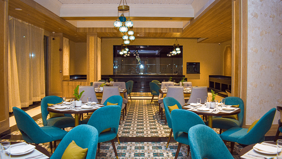 A modern restaurant interior with teal armchairs, round tables, patterned tile floor, and a distinctive globe chandelier - Urban Suites by BluSalzz, Jaipur