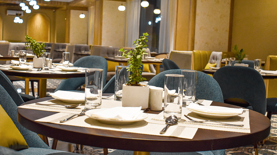 A restaurant interior with set round table, upholstered chairs, glassware, plants, and decorative lighting - Urban Suites by BluSalzz, Jaipur