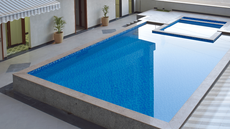 An outdoor swimming pool with blue tiles, surrounded by a concrete patio and potted plants at Urban Suites by BluSalzz, Jaipur.