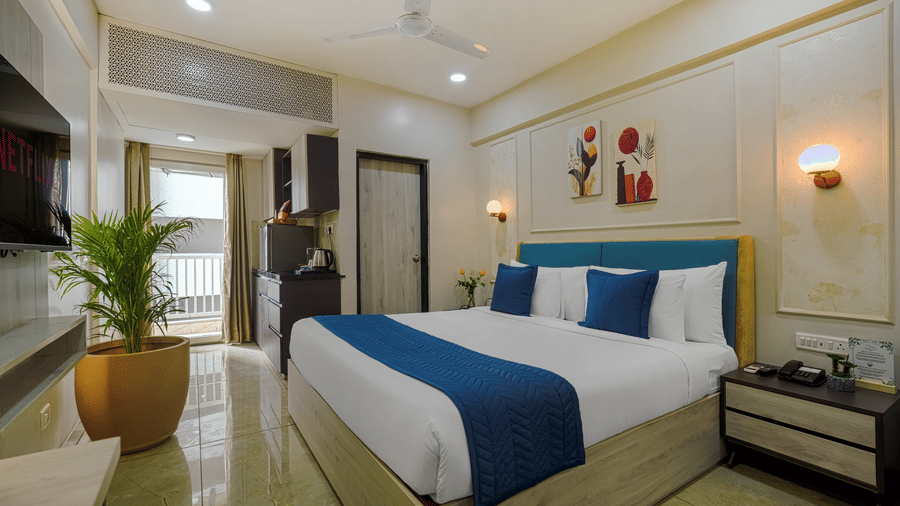 Urban Suites by BluSalzz, Jaipur's studio premium king room featuring a bed with bedding, a nightstand, and a potted plant in the corner.