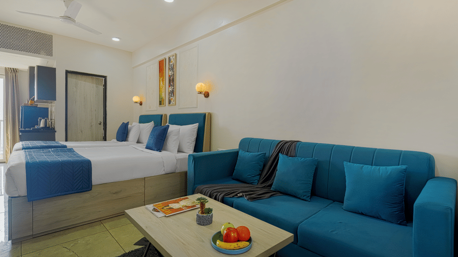A hotel room at Urban Suites by BluSalzz, Jaipur, featuring a couch, coffee table, and a bed in the background.