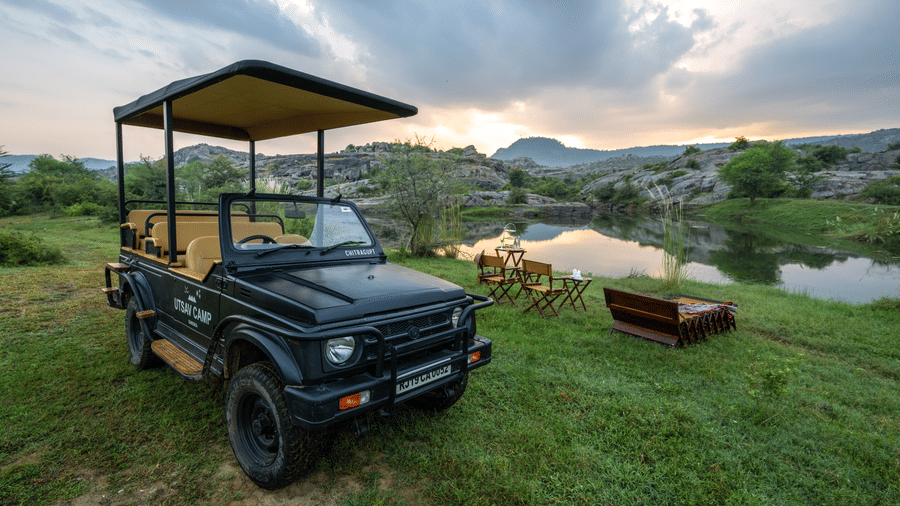 An image of a jeep parked amidst an open field with greenery - Utsav Camp Sariska