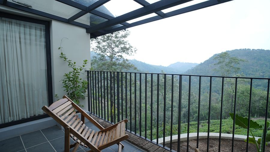  A serene balcony at Vaasta Vagamon with a wooden lounge chair, offering expansive views of lush green mountains and valleys.