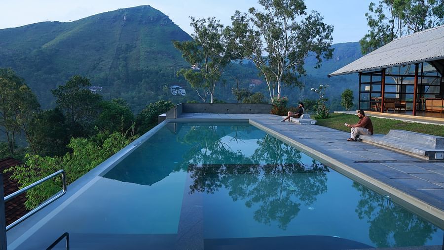 An infinity pool at Vaastha Vagamon overlooking a serene mountainous landscape, with guests relaxing on the poolside deck.