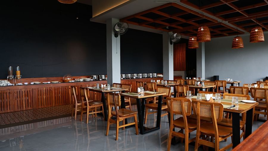  A well-appointed dining area at Vaastha Vagamon, featuring numerous tables and chairs, a buffet spread, and modern lighting fixtures.
