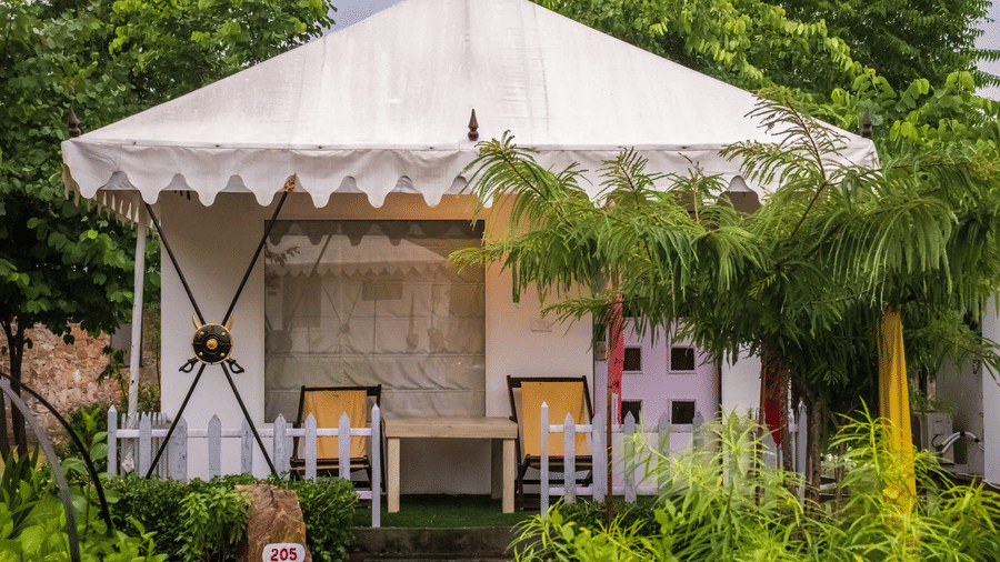 Tent accommodation exteriors amid plants and trees at Valley by Grassfield, a glamping resort in Jaipur.