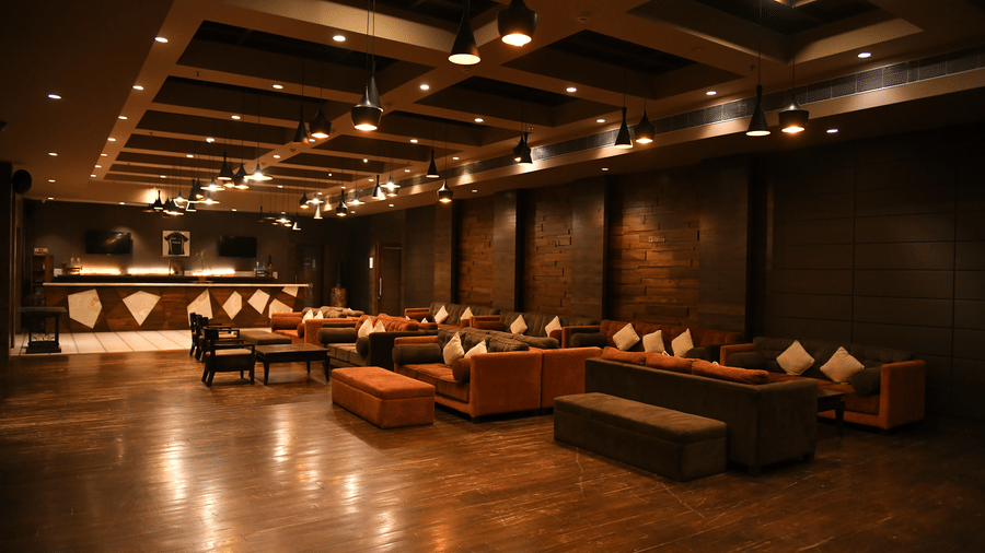 A warmly lit banquet hall at Vedic Village Spa Resort featuring low seating arrangements with cushioned sofas dark wooden flooring and ambient ceiling lighting in an intimate setting.