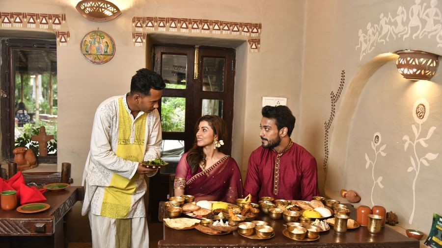 A server in traditional attire presenting food to two seated individuals at a low table | Bhoomi Restaurant