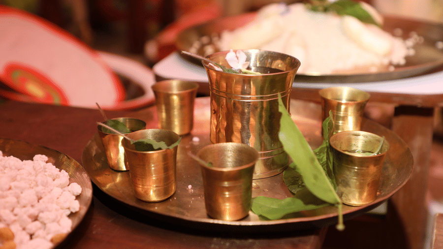 A traditional meal setup at Vedic Village Spa Resort featuring rice and side dishes served in brass utensils and plates arranged on a wooden surface with banana leaf accents.